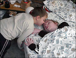 Child leaning over a second child who is lying in a bed