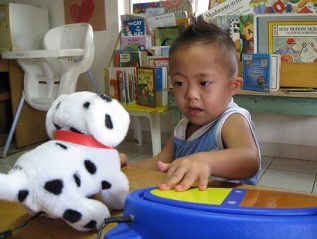 Boy using a simple switch to operate toy dog with a high chair and books in the background