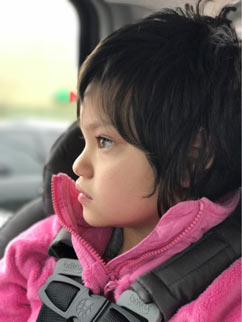 Young girl with Rett syndrome wearing a pink fleece jacket looking out of car window from her carseat
