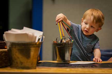 Child placing colored pencils into a bucket