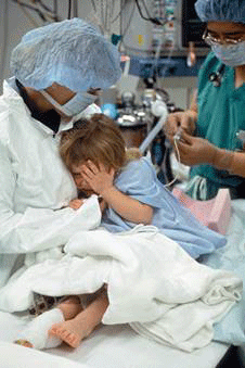 adult in protective gear comforts a child in a hospital gown in a medical setting